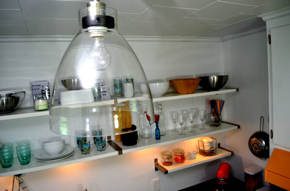 A kitchen has open shelves that hold glassware and serving bowls.
