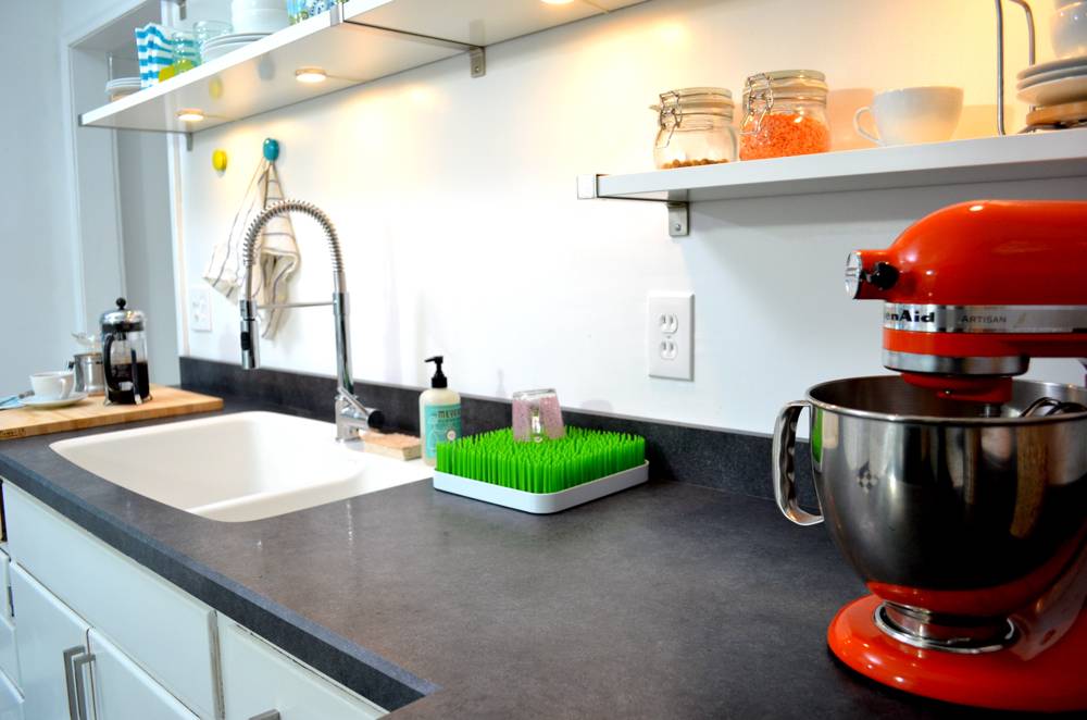Black counters and a white sink are in a kitchen with light walls.