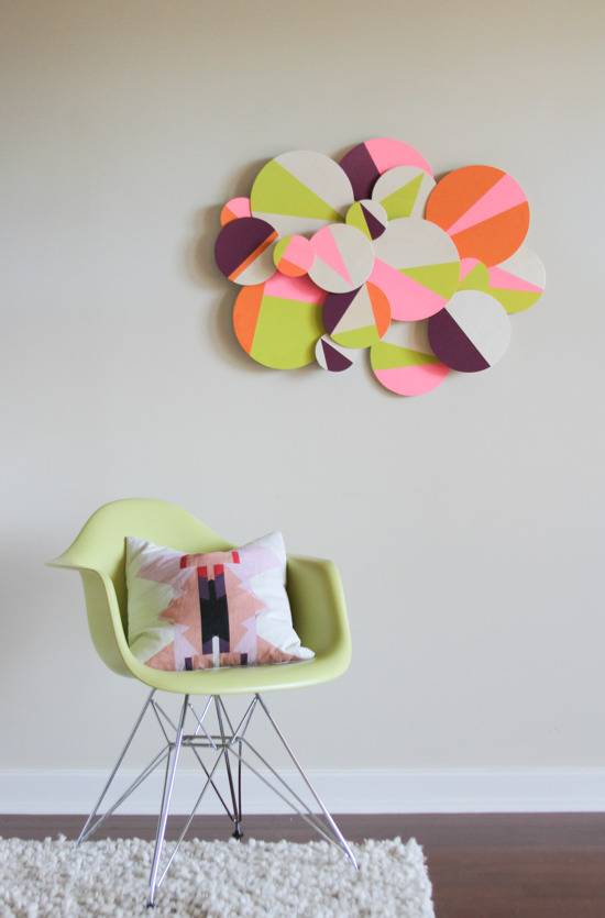 A green chair that has a white and pink pillow on it, with a wall hanging above it that matches.