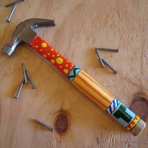 A hammer that has been decoratively painted sits on wood with some unused nails.