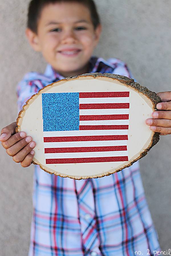 Child holding a piece of log, showing a flag painted on it.