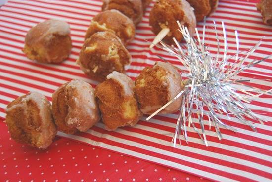 Donut holes stuck on a stick with a silver spiky decoration at the end laying on red and white striped paper.
