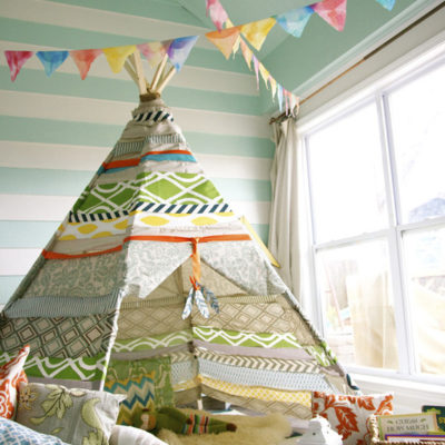 A child's room contains a teepee and streamers.