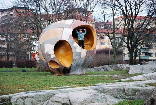 A person in a blue shirt is standing inside of a piece of art in a park.