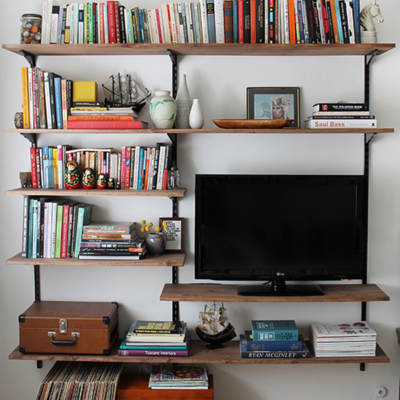 Books are lining shelves near a television near a white wall.