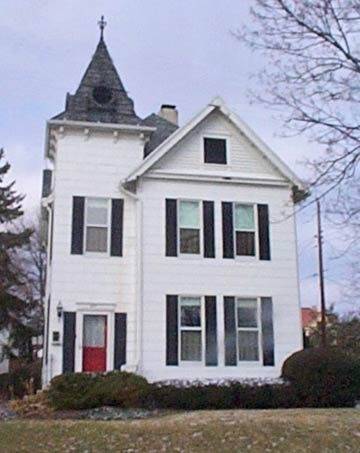 A white two story house with a red door and a cross on the rooftop.