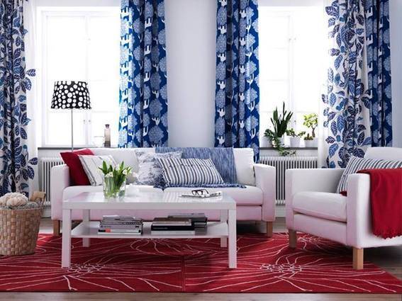 A white couch, chair, and table in a room that has a red carpet and blue curtains.