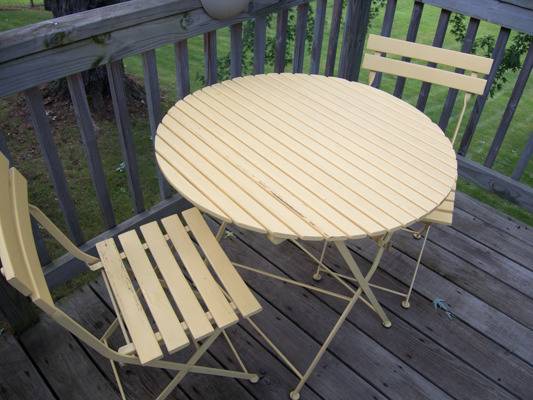 A small, round, slatted outdoor dining table and chairs sit on a deck.