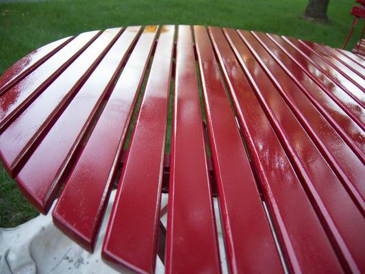 A slatted red table that is sitting in a park.