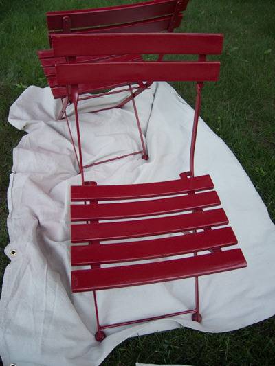 A red chair is sitting outside on a white piece of material.