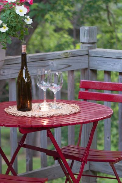 A red wood table that is on a porch with wine glasses and wine.