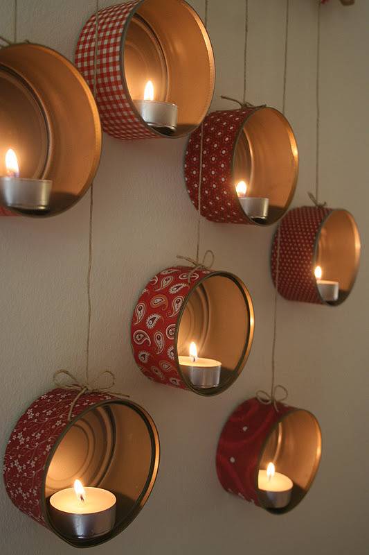 Short metal cans with fabric coverings and tea candle lights on a wall.