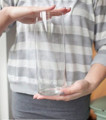 A cylindrical clear glass container is being held by a person.