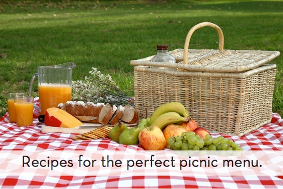 A picnic with grapes, orange juice, a basket and apples on a blanket.