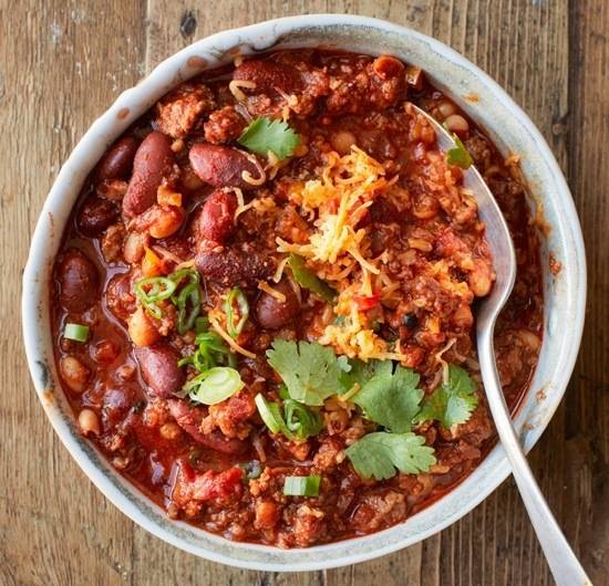 Chili with beans, cheese, and cilantro in a bowl with a spoon.