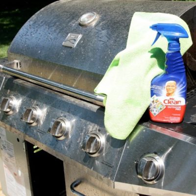 Bottle of spray cleaner with a rag on top of a stainless steel grill.