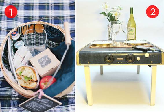 Picnic basket on a blanket and folding table set for a meal.