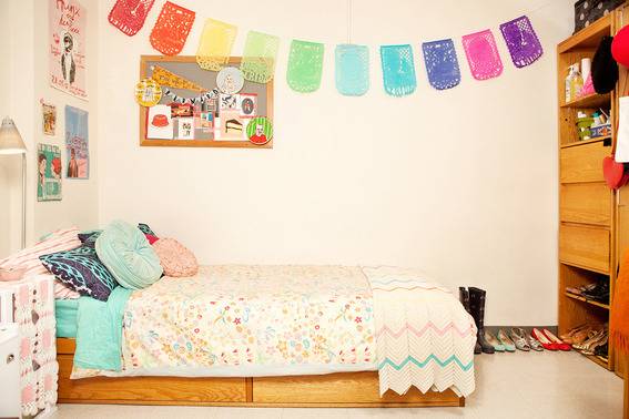 Dorm room with cot and colorful hanging arch on side wall.