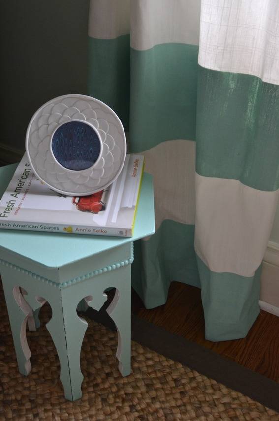 A book is sitting on a light blue table near a blue and white curtain.