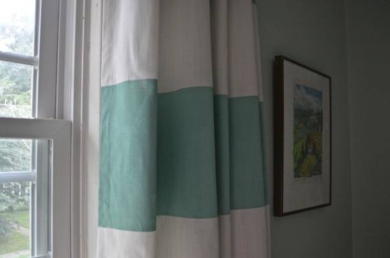 A white curtain with a green broad horizontal stripe hangs on a white window.