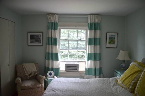 A room has teal and white curtains and yellow pillows.