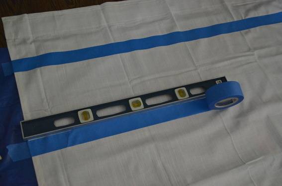 A piece of white cloth with a blue stripe, a level laying on the cloth next to a strip of blue tape.