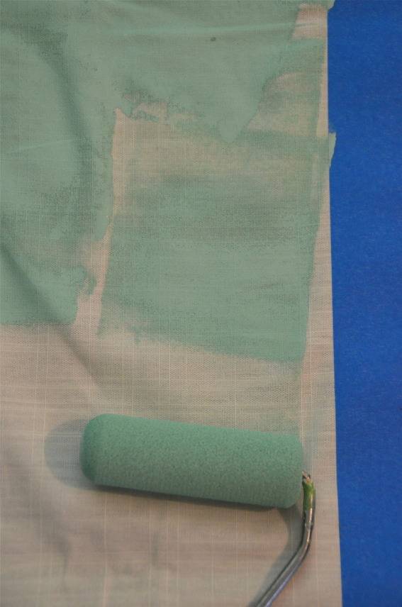 A lime green paint roller paints on a white surface with blue tape on it.