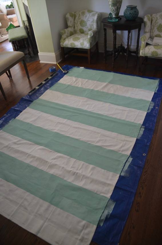 A green and white horizontally striped sheet on top of a blue blow up matress.