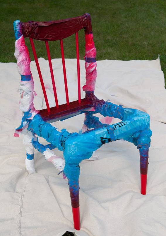 Wooden chair wrapped with cloth ribbons on top of drop cloth.