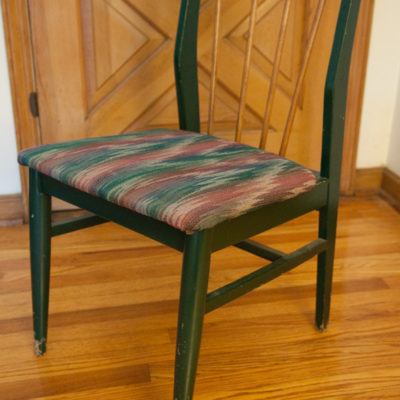 A dining chair is green except for wood-color back slats.
