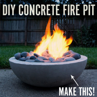 A concrete fire pit contains rounded stones and a fire.