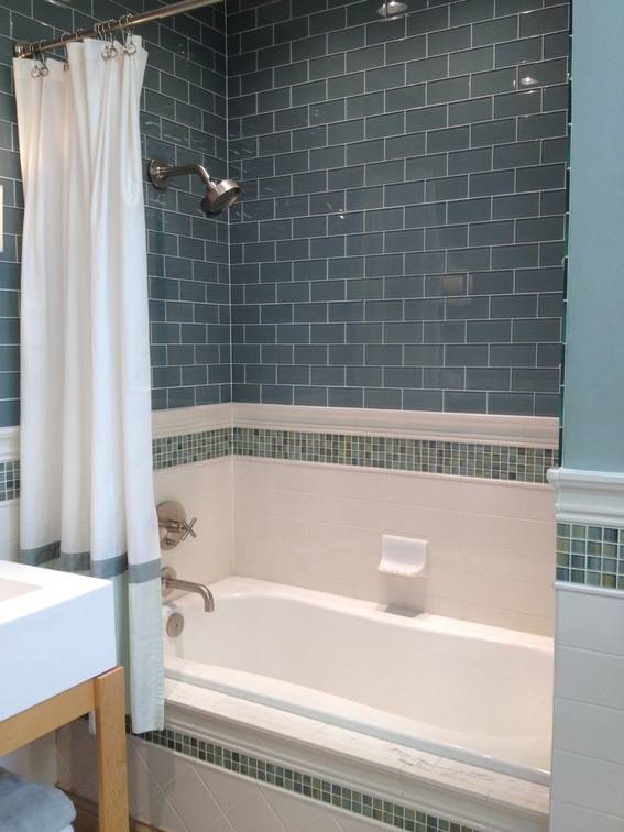 A white bathtub with a blue tiled wall and a white curtain.
