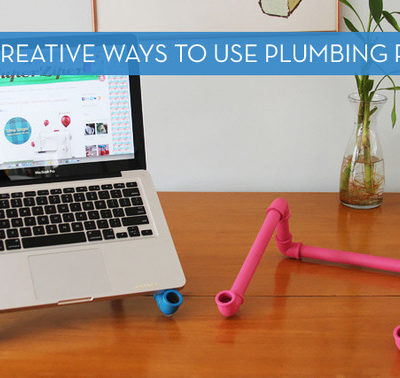 A laptop stand has been created using plumbing pipe and is displayed on a desk with a vase.