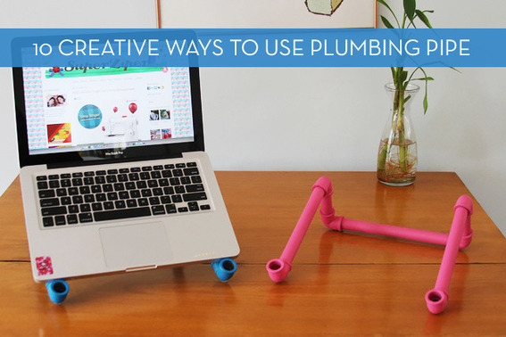 A laptop stand has been created using plumbing pipe and is displayed on a desk with a vase.
