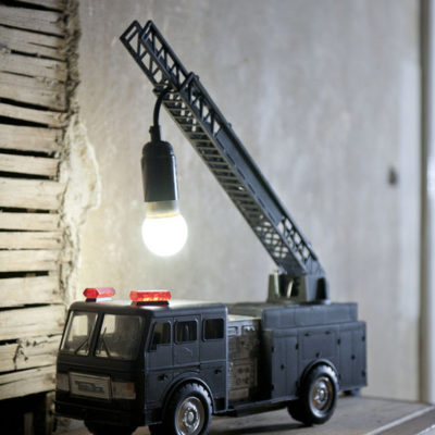 A black toy firetruck with a light bulb hanging from it, being used as a lamp.