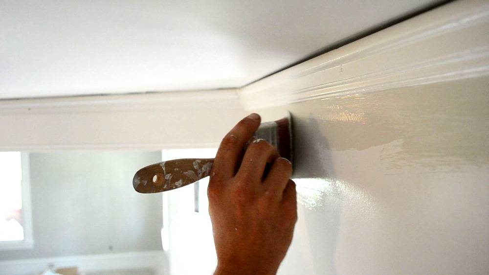 A person is using a paintbrush near the wall near the top moulding.
