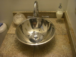 A silver bathroom sink raised bowl on a tan marble counter with a soap dispenser and a stainless steel faucet.