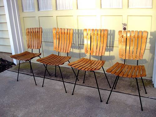 Four brown slat chairs on black legs in front of a garage door.