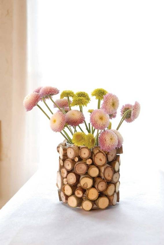 A vase made of small wooden circles that has pink and yellow flowers in it.