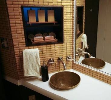 A sink sits on a white counter near a mirror and a tan tiled wall.