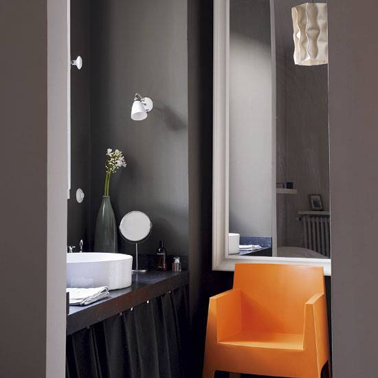 A black bathroom that also has an orange chair sitting in it.