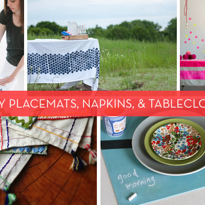 A woman painting, a blue table cloth on a table in a grassy field, a pink table cloth on a table, napkings with tassles, a colorful plate on a green plate on a grey palte on a blue placemat that has good morning written in chalk.