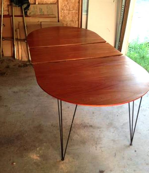 A long, oval, wooden dining table with black metal legs sitting in a garage.