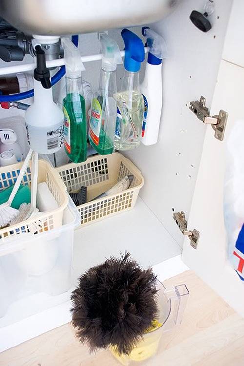 Cleaners are hanging on a rod under a sink.
