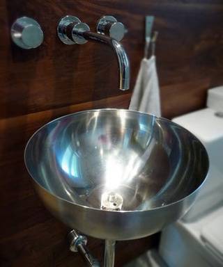 Metal bowl with legs near a faucet in a bathroom.