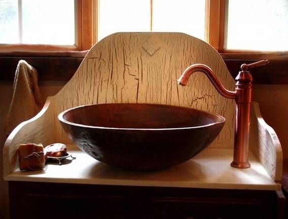 Metal bowl converted to a sink next to a faucet on top of a wood stand.