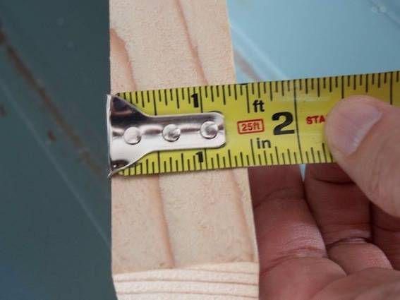 A hand using a measuring tape to measure a one inch piece of wood.
