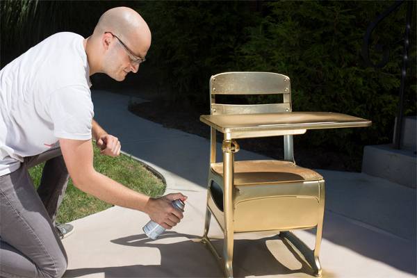 A man spray painting an old wooden school desk.