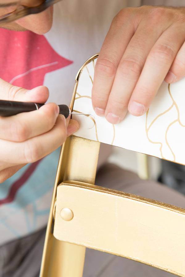 A person's hand drawing on the back of a beige chair.