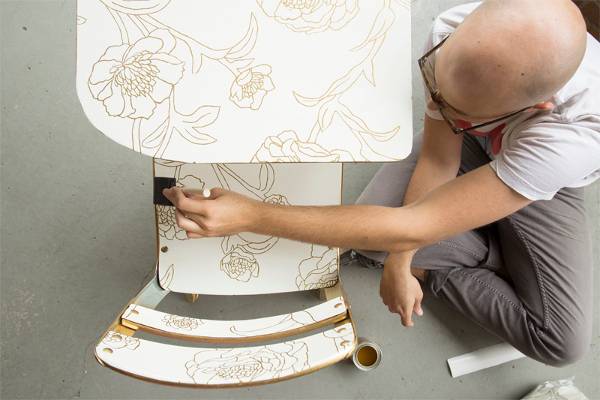 A man using a sponge brush to apply wallpaper to an old school desk.